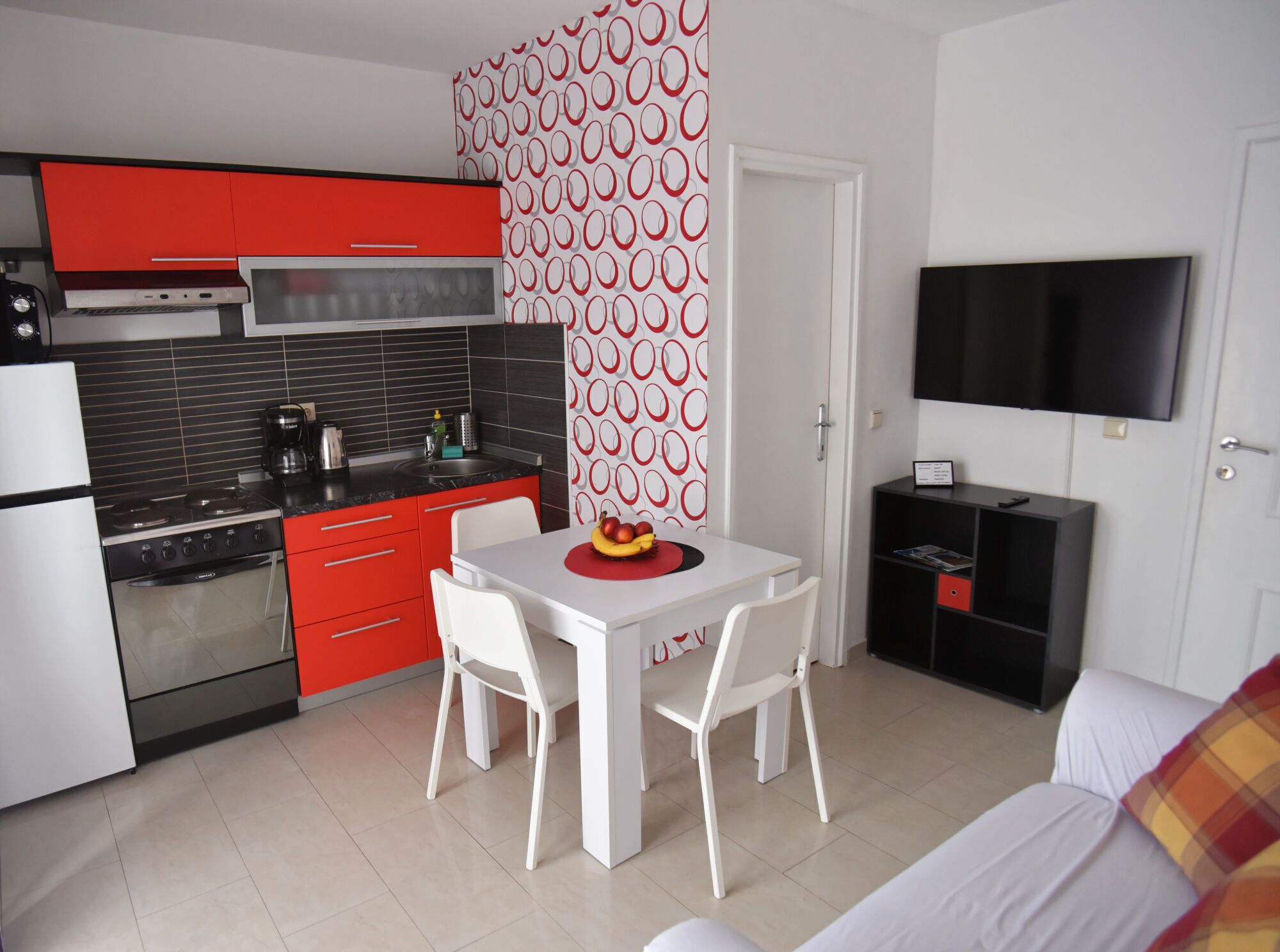 Een compacte keuken met moderne apparaten, een eethoek met een tafel en stoelen, en een aan de muur bevestigde televisie.