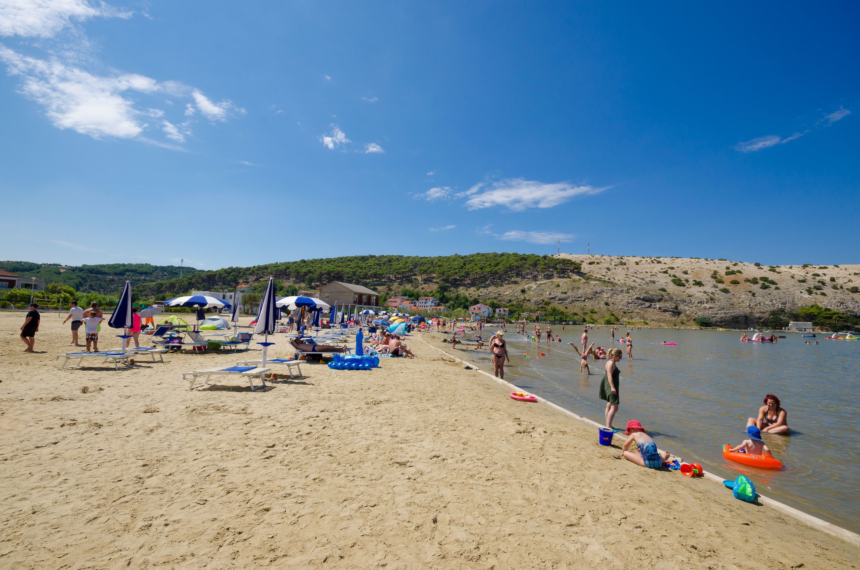 A beach with sun loungers, umbrellas, and people swimming.