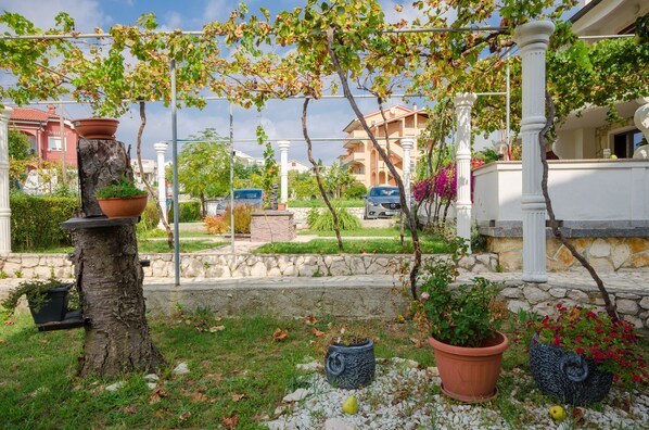 A garden with potted plants, a tree, and a stone wall. - Apartments Helena (Lopar)