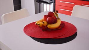A kitchen with red cabinets, a stove, and a table with a fruit arrangement. - Apartments Helena (Lopar)