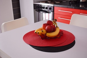 Een keuken met rode kastjes, een fornuis en een tafel met een fruitschaal.