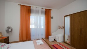 A bedroom with a bed, a bedside table with a lamp, a wooden wardrobe, a small stool, and a fan. - Apartment Milja (Banjol)
