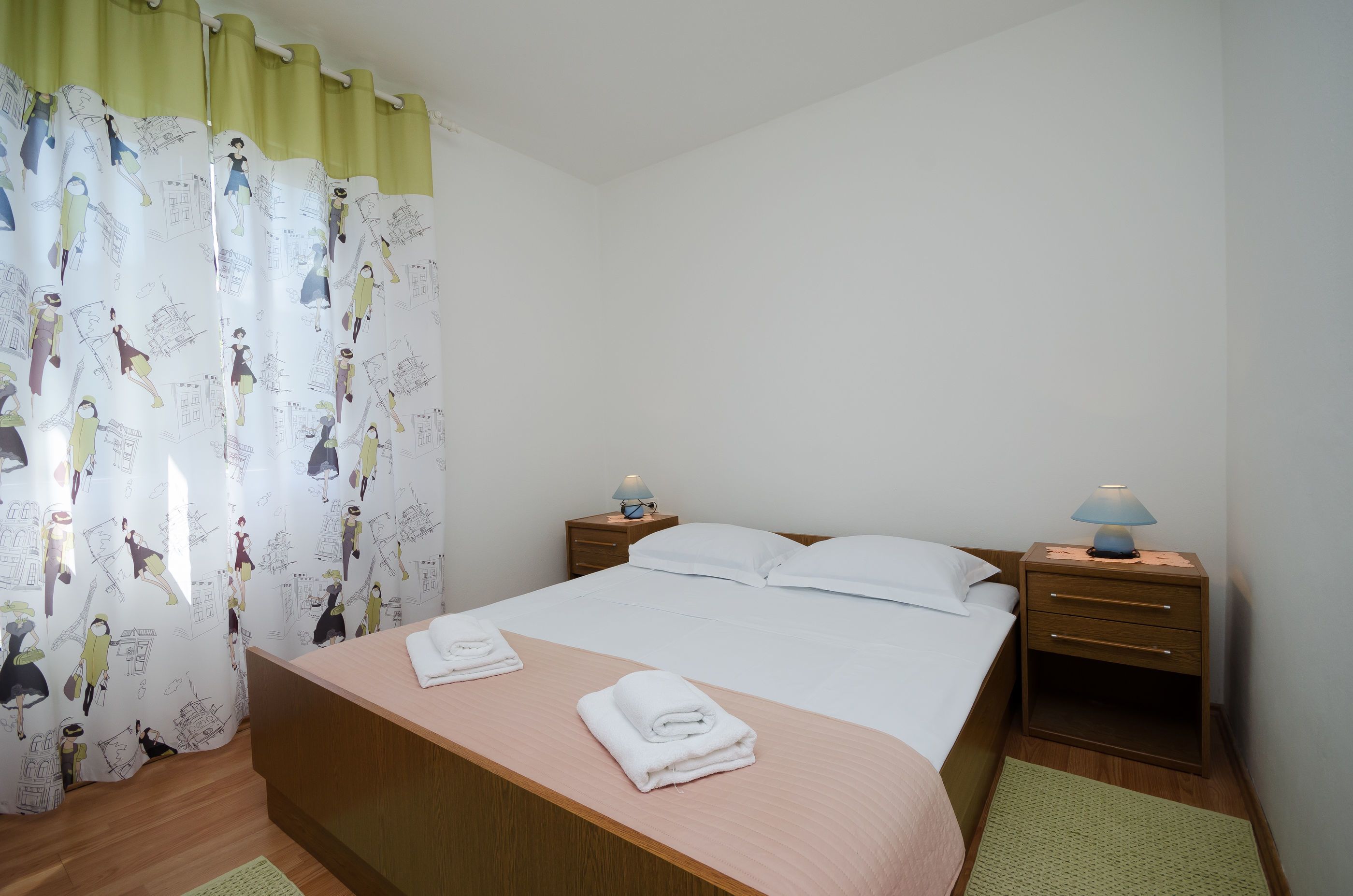 Une chambre d’hôtel avec un lit, deux tables de chevet avec des lampes, un tapis vert et un rideau orné de personnages de dessins animés.