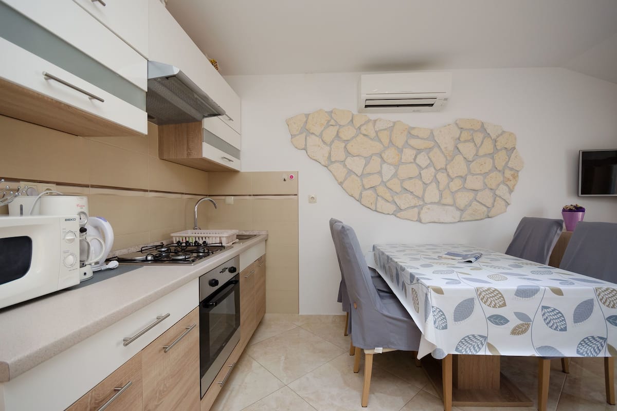 Cocina compacta con microondas, estufa y horno, una mesa de comedor con sillas, y un adorno de pared de piedra.