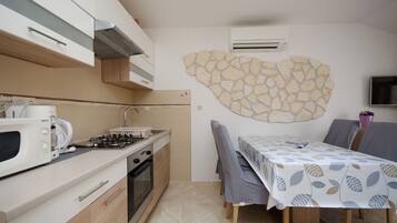 A compact kitchen with a microwave, stove, and oven, a dining table with chairs, and a stone wall decoration.