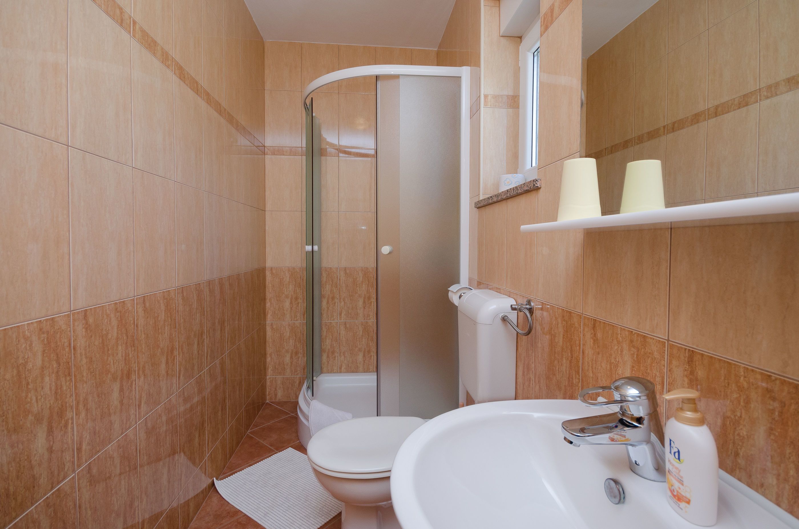 Une salle de bain équipée d’une douche, de toilettes, d’un lavabo et d’étagères de rangement.