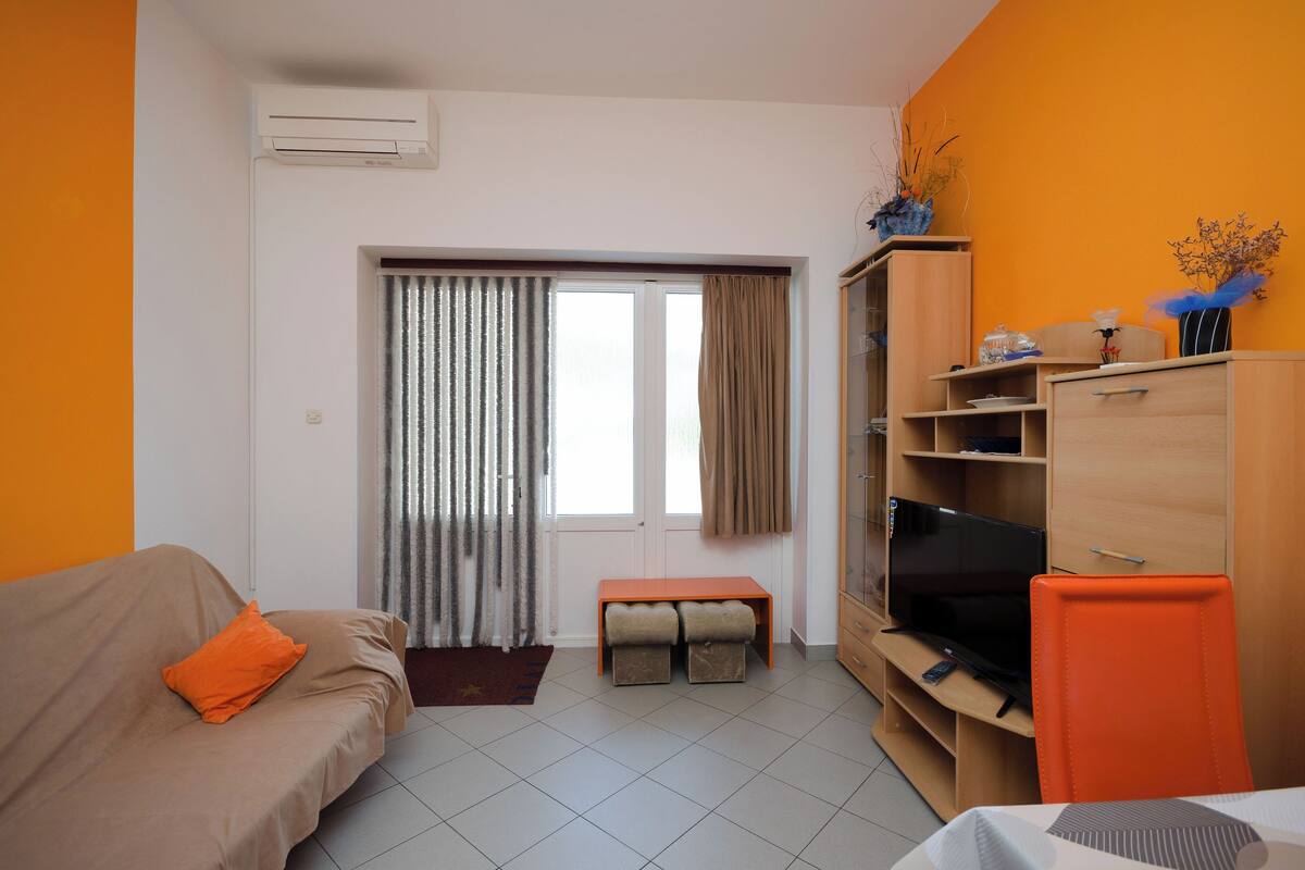 Una sala de estar con sofá, reposapiés, mueble para televisión y un armario.