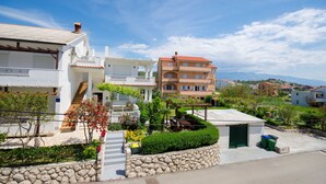 A residential area with a white building with a staircase, a beige building with a red roof, and a stone wall with greenery. - Apartments Mirjana (Lopar)