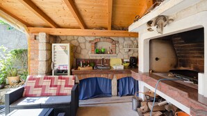 A rustic outdoor kitchen with a stone fireplace, wooden beams, and a stone wall. - Apartments Mirjana (Lopar)