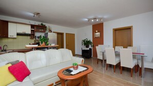 A modern living room with a sofa, coffee table, and dining area with chairs. - Apartments Mirjana (Lopar)