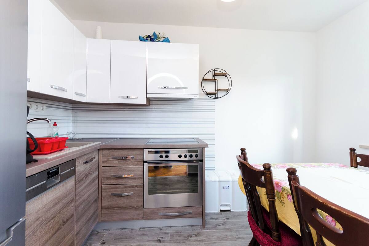 A compact kitchen with modern appliances, wooden cabinetry, and a dining area with a table and chairs.