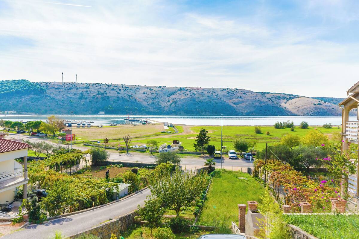 A residential area with a view of a lake, a road, and a hilly landscape in the background.