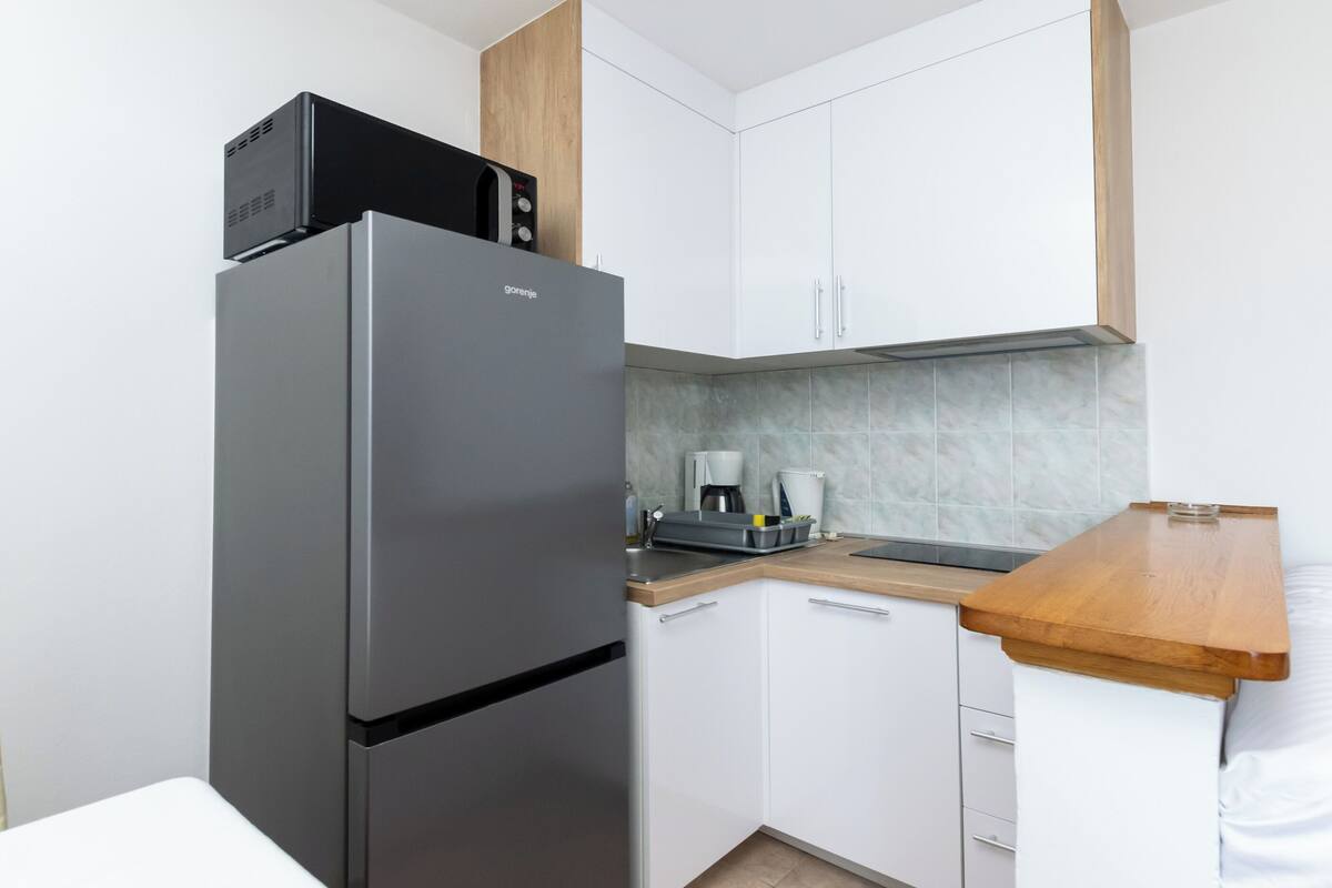 A compact kitchen with a stainless steel refrigerator, a microwave, and a coffee maker on the countertop.