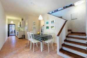 A dining area with a table set for four, white chairs, a hanging light fixture, and a staircase leading to an upper level. - House v (Lopar)