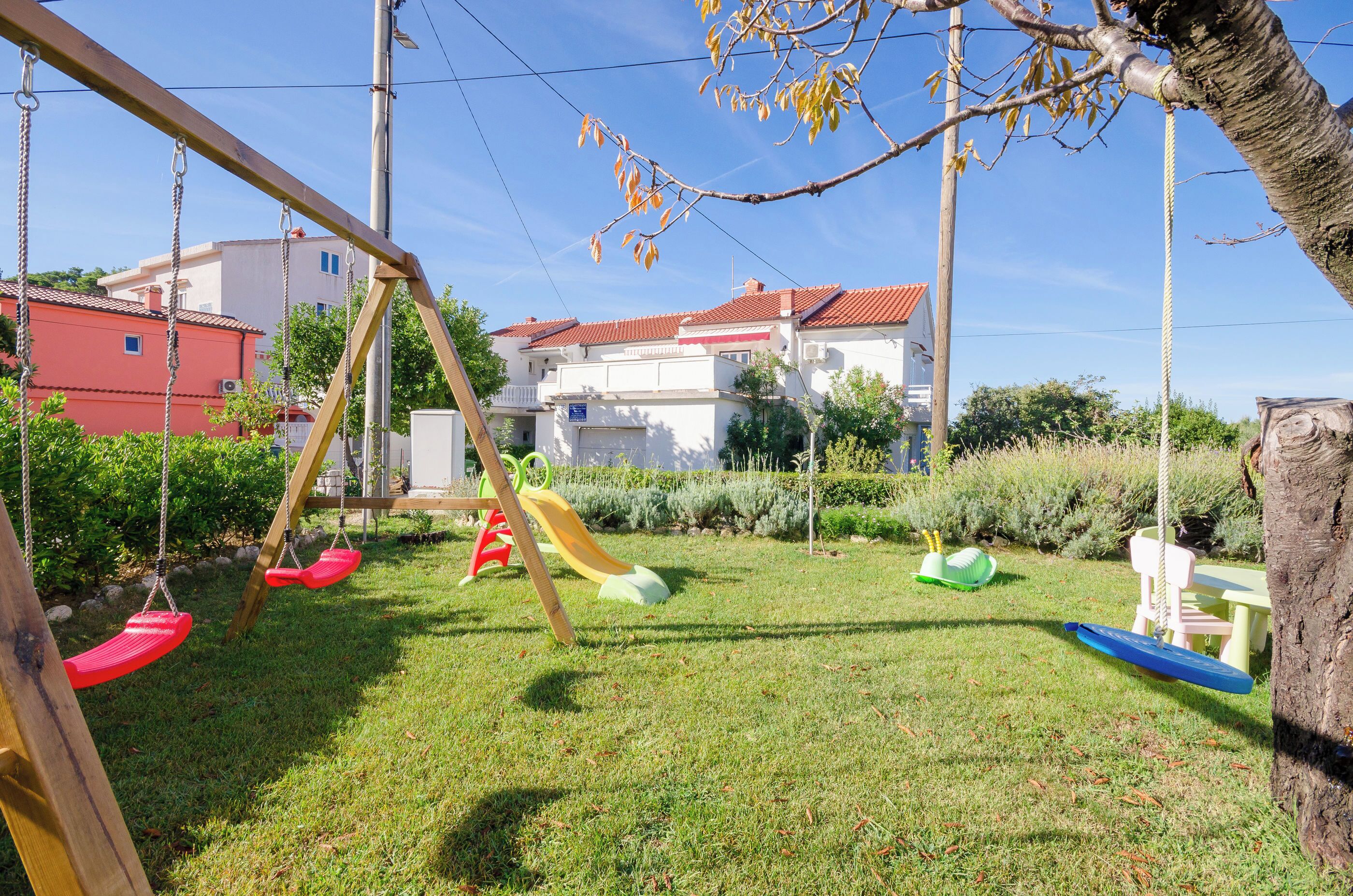 A playground with swings and a slide, surrounded by grass and trees.