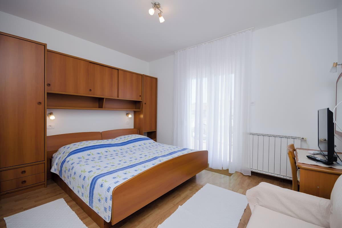 Ein Schlafzimmer mit einem hölzernen Bett, einem Schreibtisch mit Computer, einem Stuhl und einer Heizung.