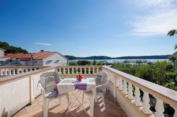 A balcony with a table and chairs, overlooking a body of water and greenery. - Rooms Lili (Palit)
