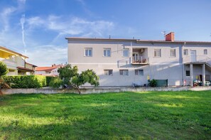 Ein mehrgeschossiges Gebäude mit flachem Dach, einem Balkon und einer kleinen Grünfläche davor.