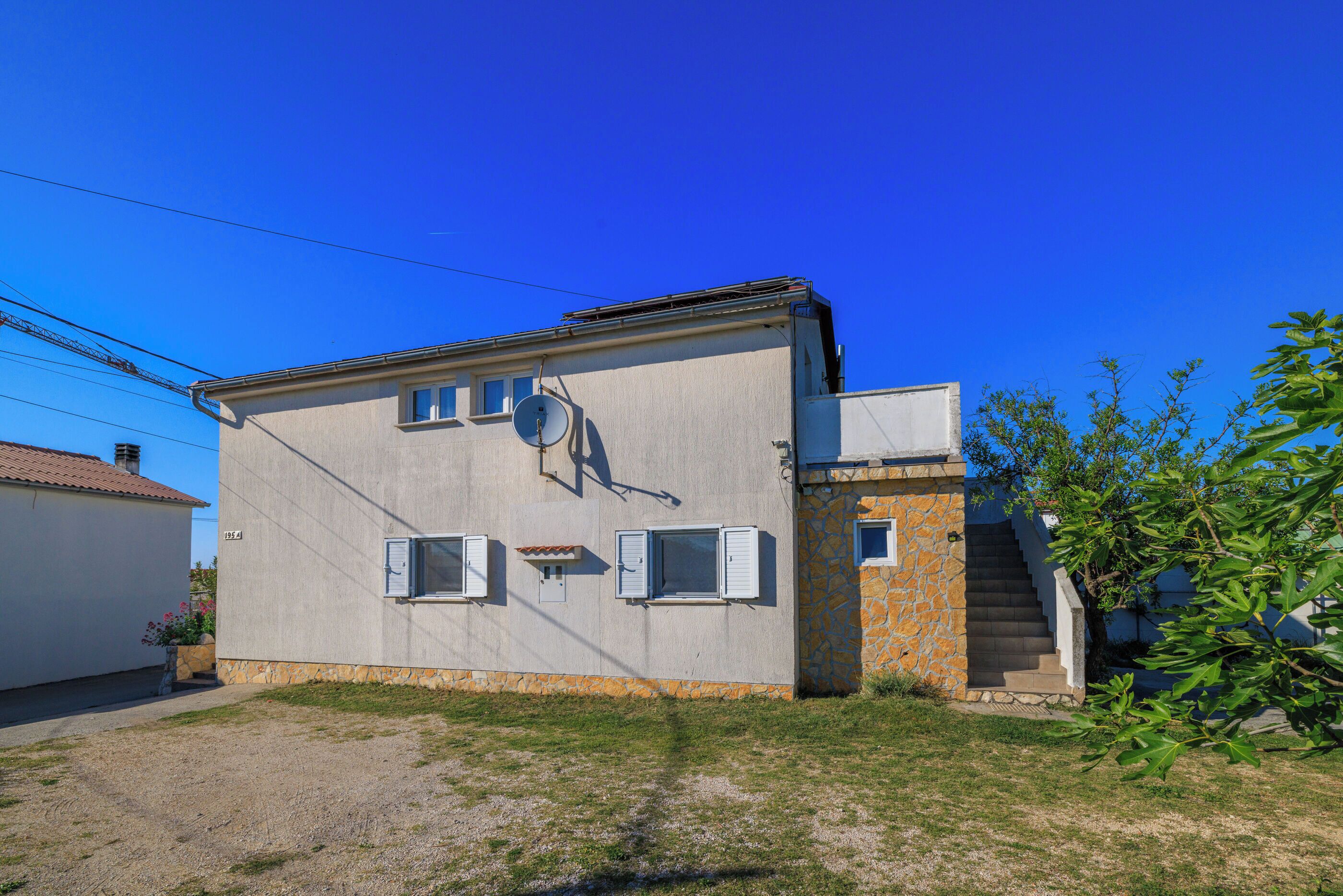 A two-story building with a stone staircase, a satellite dish, and a small garden area.