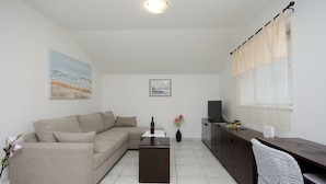 A living room with a sofa, a coffee table, a TV, and a dining area with a chair. - Apartments Slobodanka (Lopar)