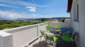 A balcony with a table and chairs, overlooking a scenic landscape with houses and mountains. - Apartments Slobodanka (Lopar)