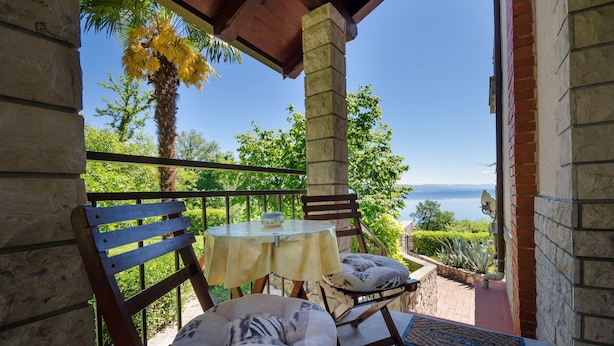 A balcony with a table and chairs, overlooking a scenic view of the sea and greenery. - Apartments Zeljko (Lovran)