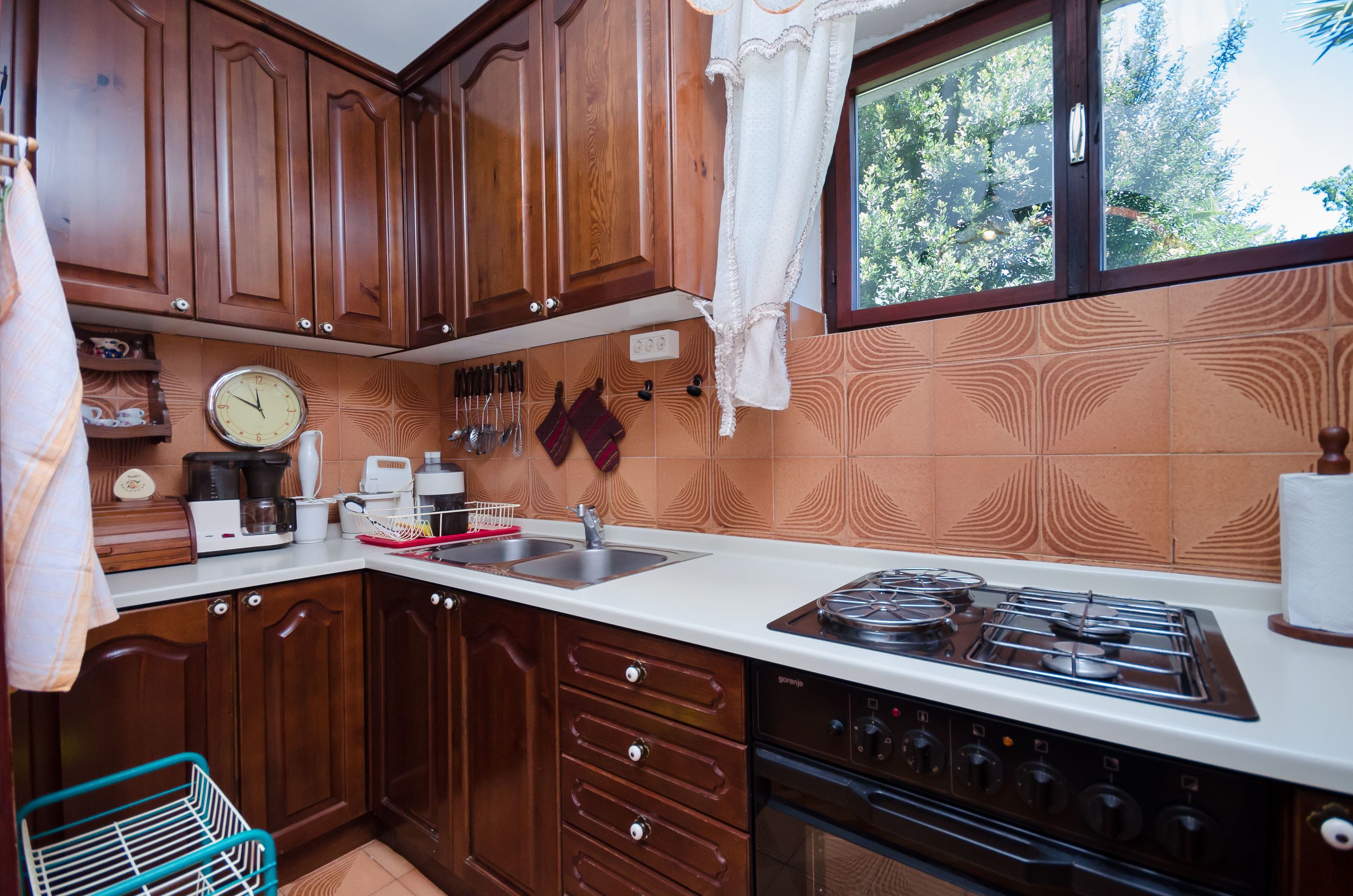Una cocina con armarios de madera, estufa, lavaplatos y ventana con vistas a árboles.