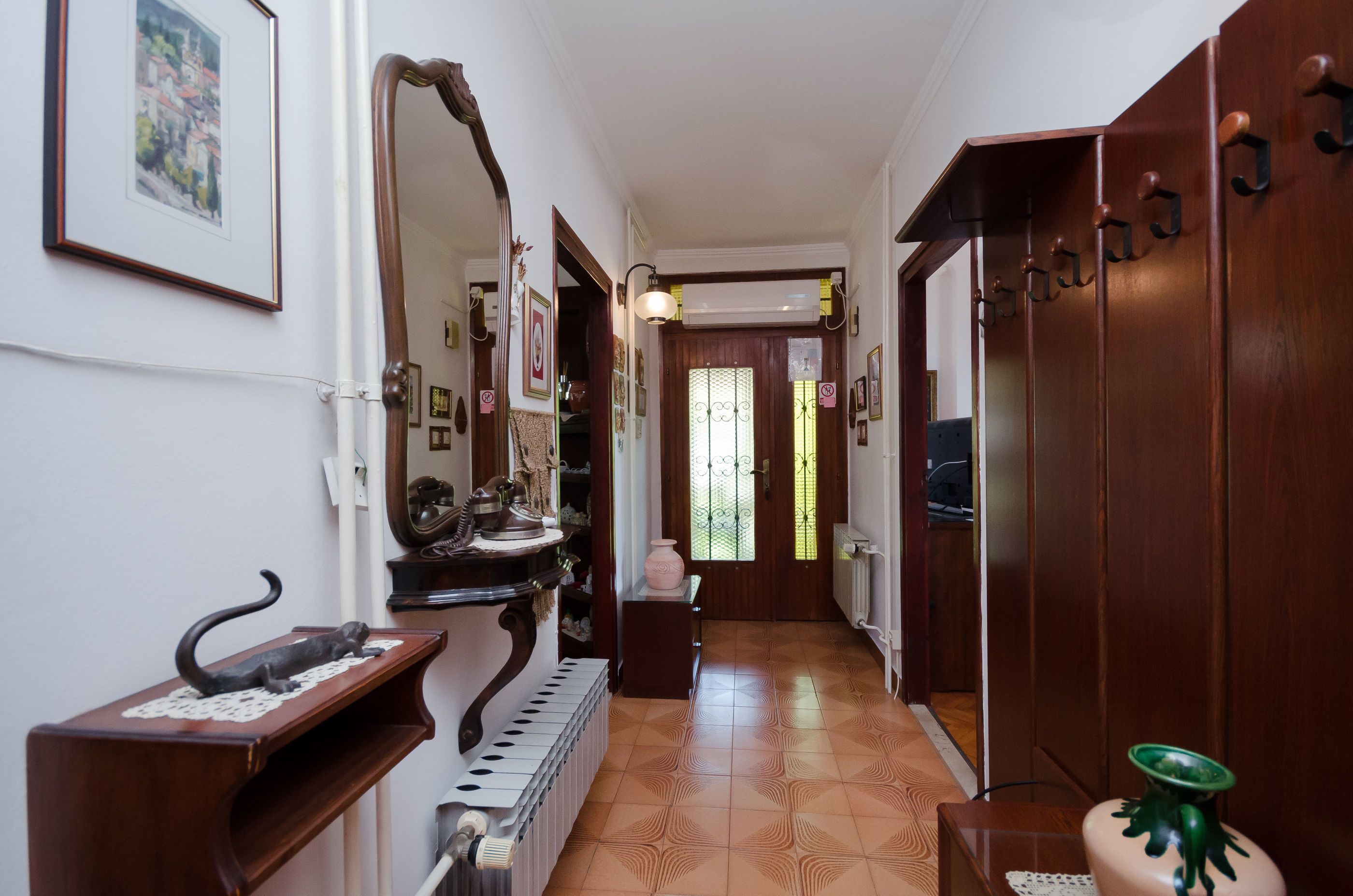 Un pasillo con suelo de madera, un radiador, un espejo y una puerta con ventanal.
