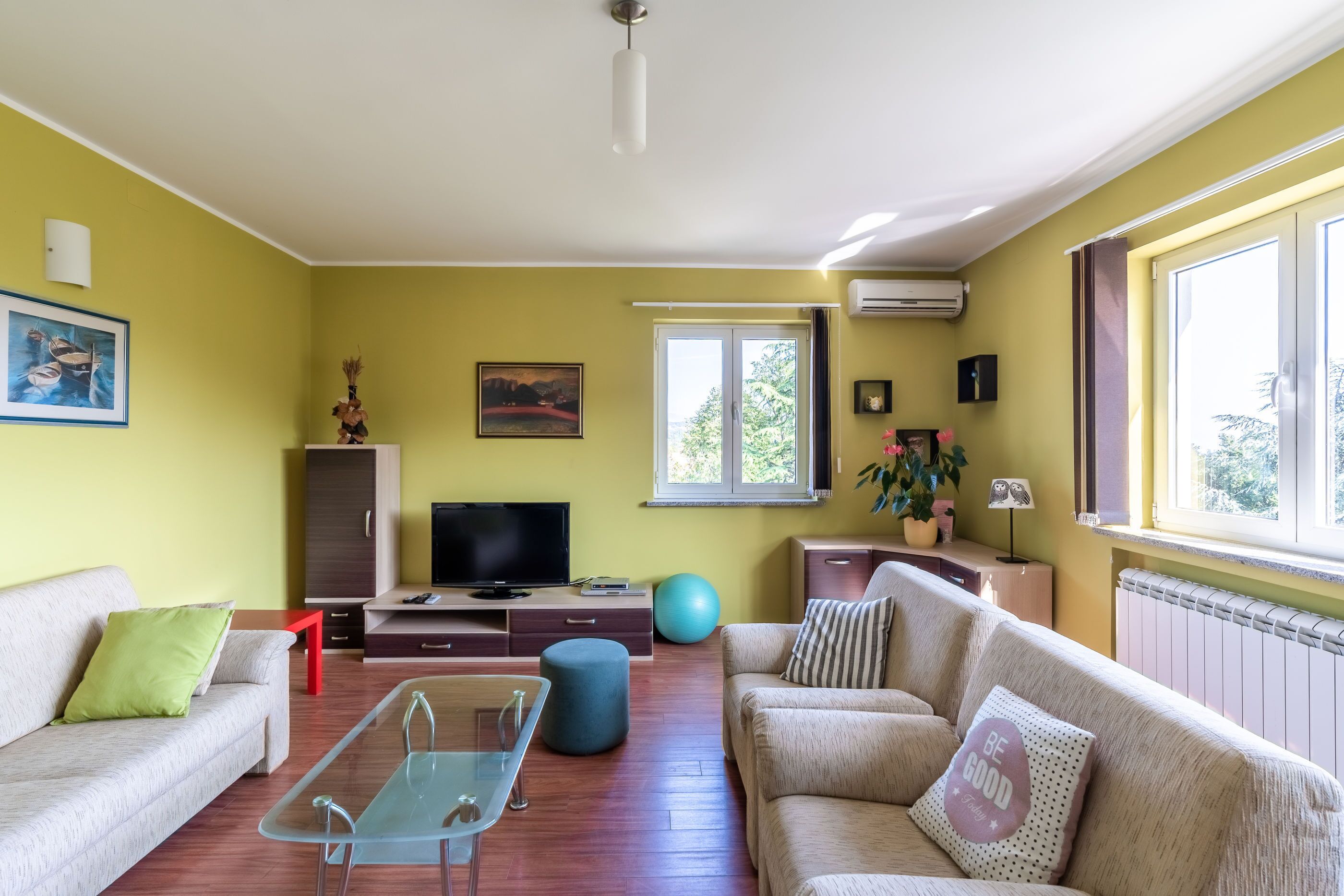 A living room with a sofa, a TV, a glass coffee table, and a window with curtains.