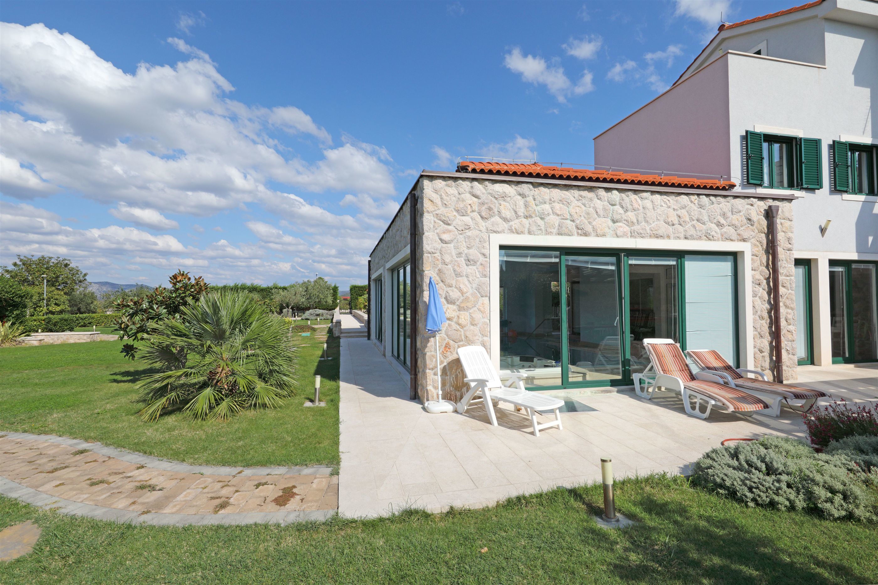 Una casa moderna con facciata in pietra, ampie porte in vetro e un patio con poltrone relax.