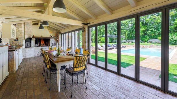 Une cuisine spacieuse avec une grande table à manger, un sol en pierre et une vue sur un jardin avec une piscine.