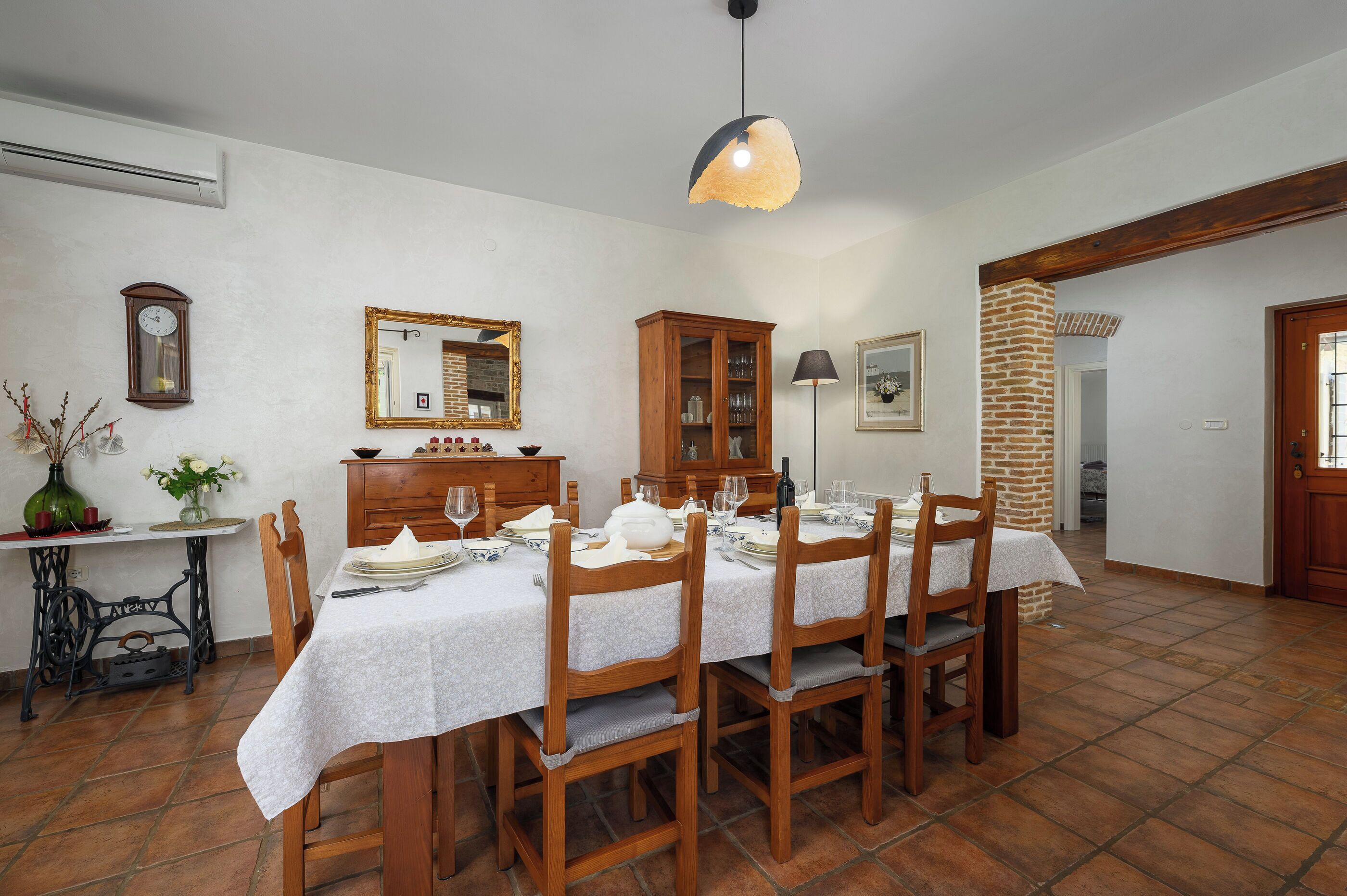 A dining area with a table set for six, wooden chairs, a cabinet with glass doors, a mirror, and a hanging light fixture.