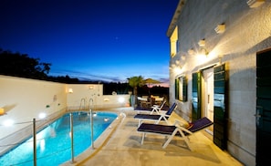 A swimming pool with lounge chairs and a building with green shutters.