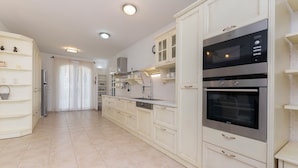 A modern kitchen with white cabinetry, stainless steel appliances, and a tiled backsplash. - Villa Serena (Mirca)