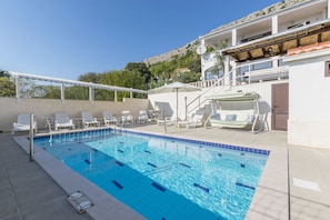 Una piscina con agua azul cristalina, sillas de descanso blancas y una pérgola blanca.