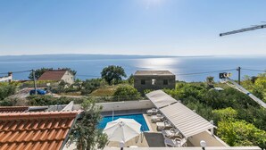 Zona de piscina en la azotea con vistas despejadas al mar, rodeada de edificios y vegetación.