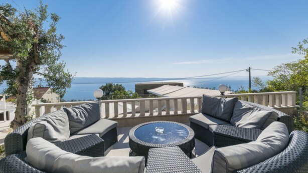 Un espacio al aire libre con luz solar, con una mesa redonda y sillas acolchadas, con vista a un paisaje panorámico.