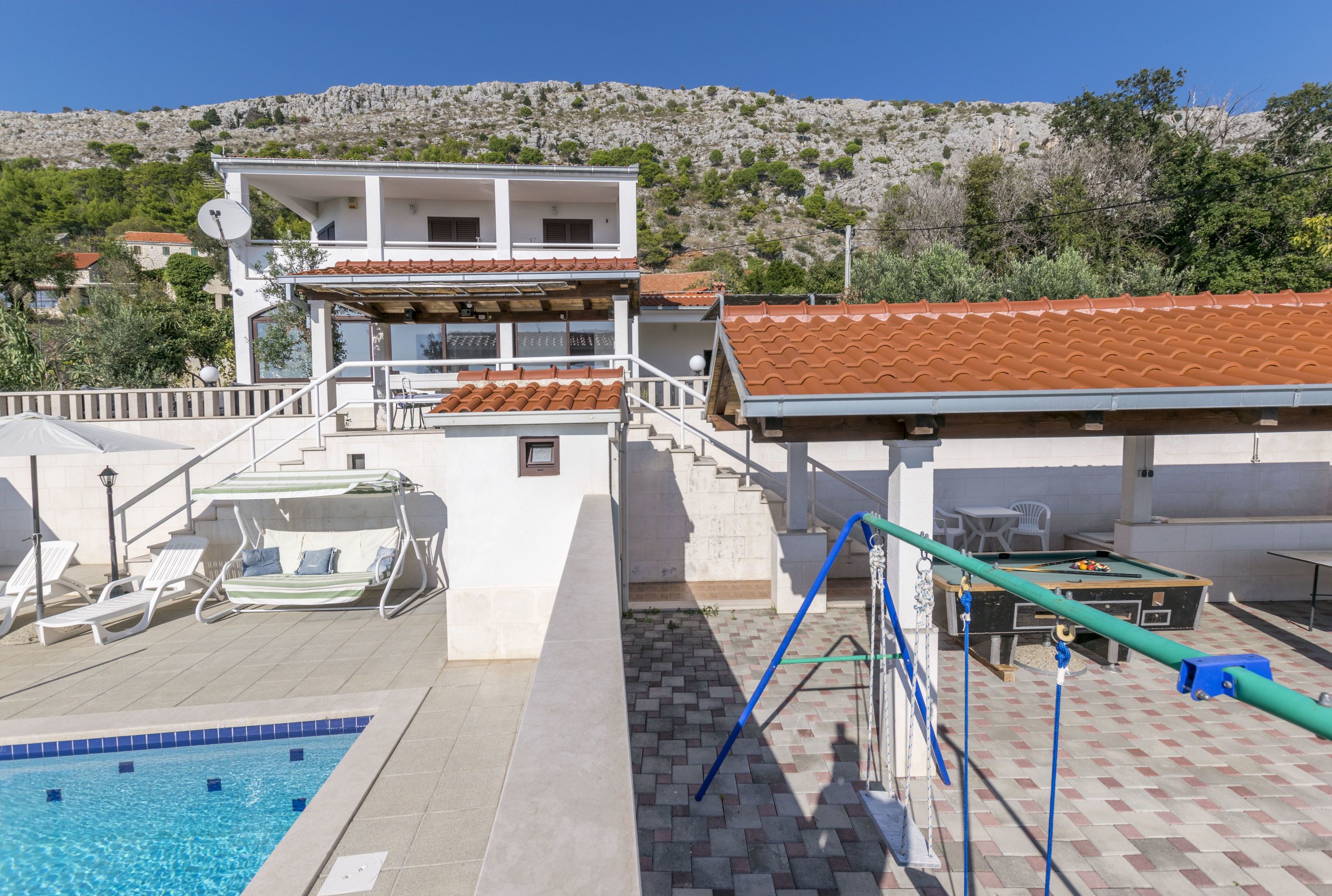 A pool area with a diving board, lounge chairs, and a pool table.
