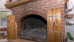 Horno de ladrillo con las puertas abiertas, un estante de madera encima y pared de ladrillo.