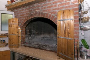 Horno de ladrillo con las puertas abiertas, un estante de madera encima y pared de ladrillo.