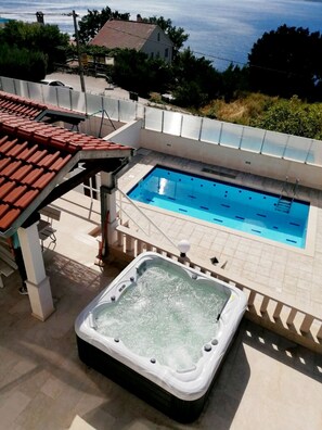 A swimming pool with a hot tub, surrounded by a white tiled deck and a red-tiled roof. - Villa Leo (Jesenice)