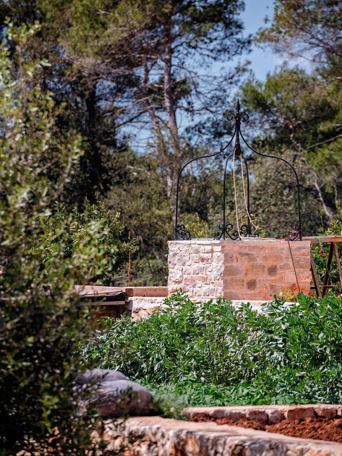 A rustic outdoor area with a stone wall, metal fence, and greenery.