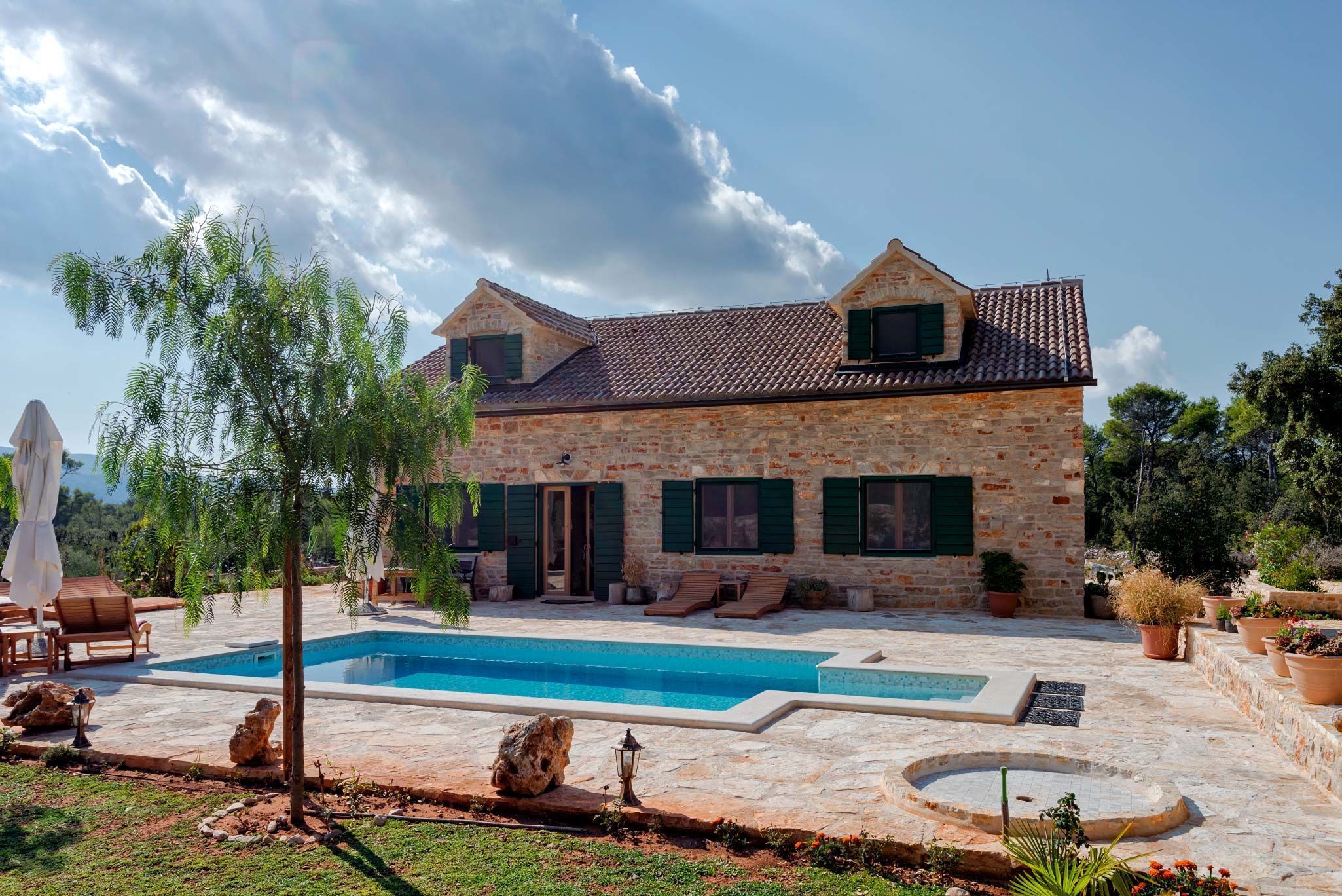 Une maison en pierre avec une piscine, un espace salon extérieur et des plantes en pot.