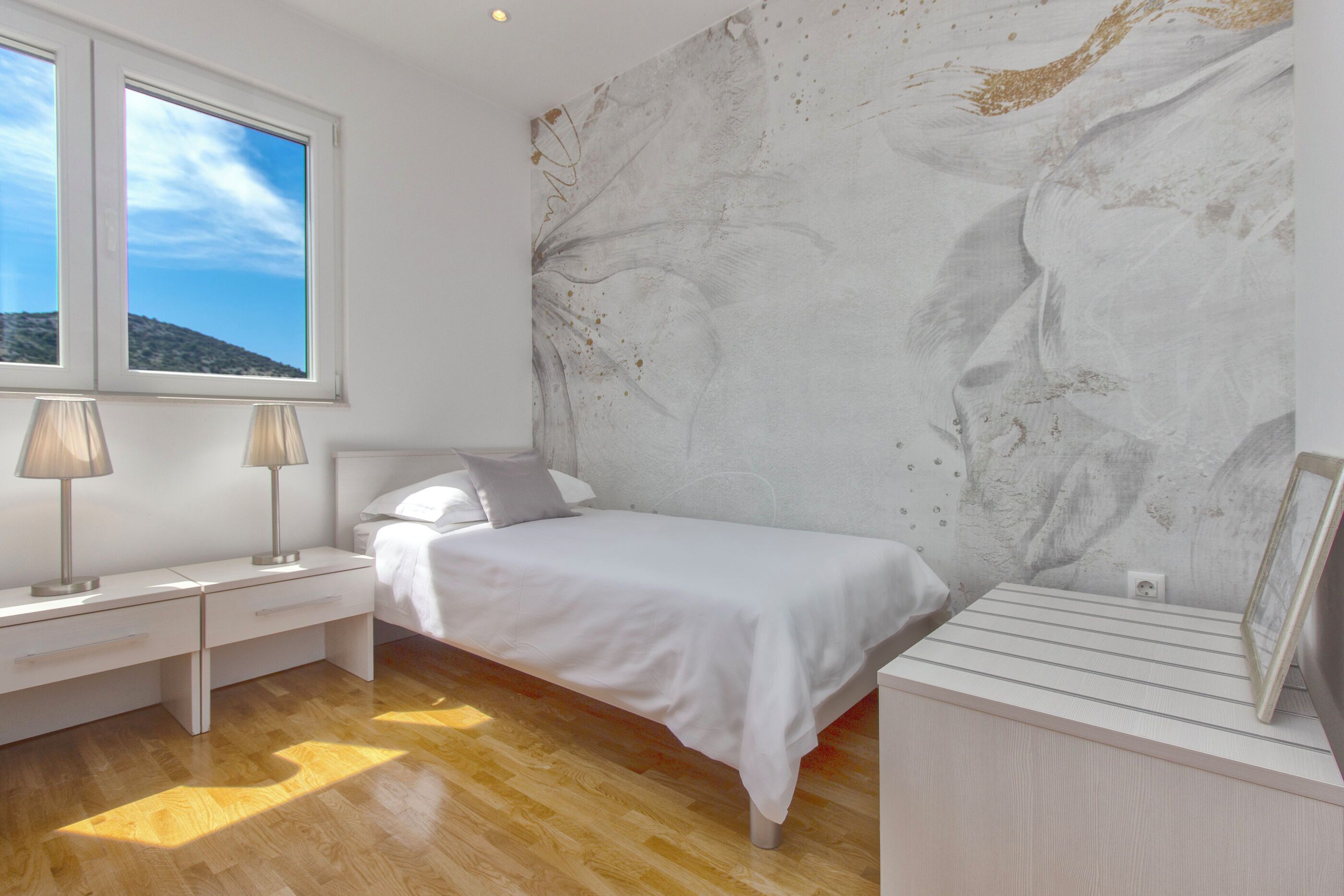 A bedroom with a bed, two bedside tables, a window, and a wall with a textured design.
