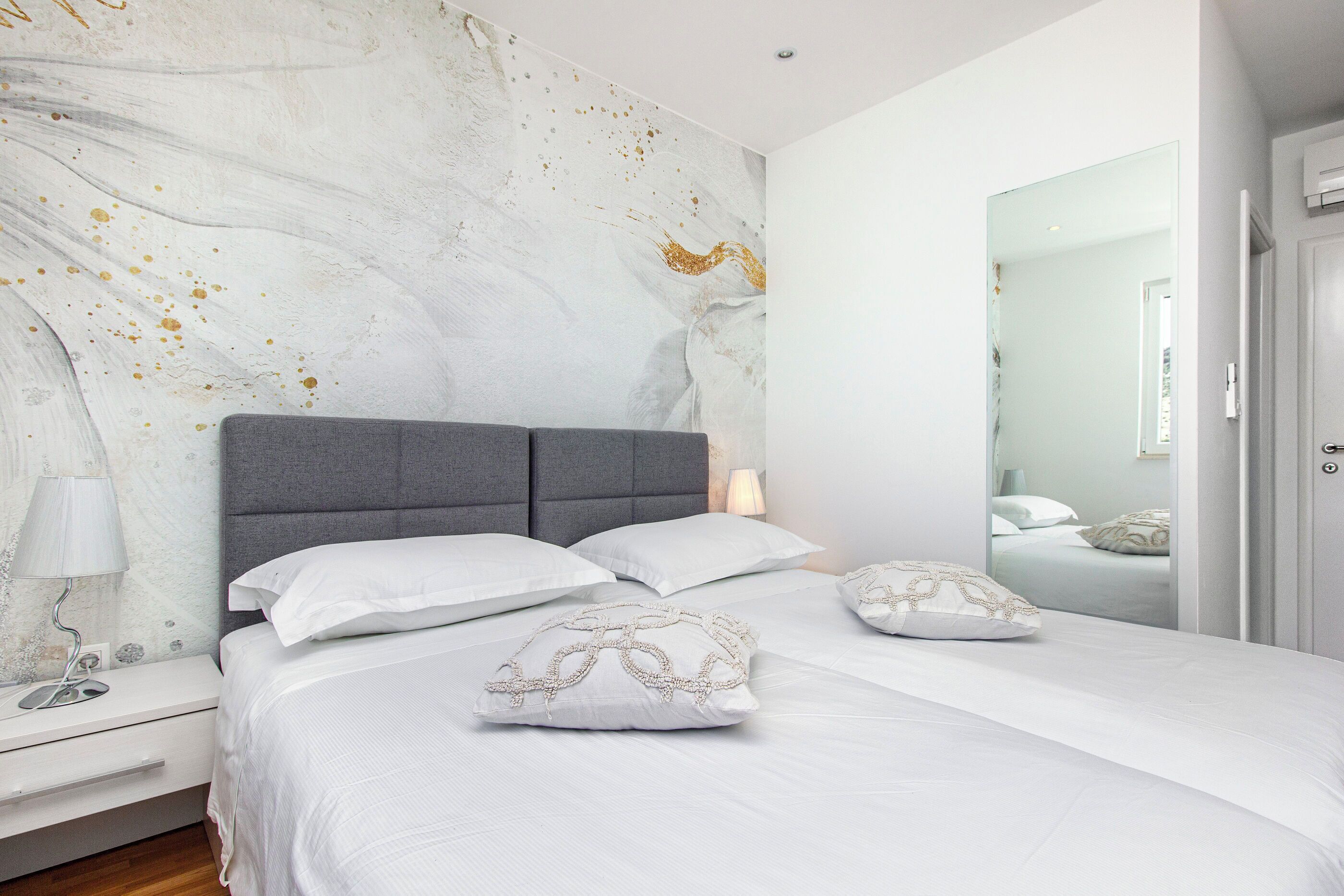 A modern bedroom with a marble wall, a grey headboard, and white bedding.