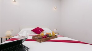 Ein Hotelzimmer mit Bett, Obst und Saft auf einem Tablett, einem Laptop und einer Lampe.
