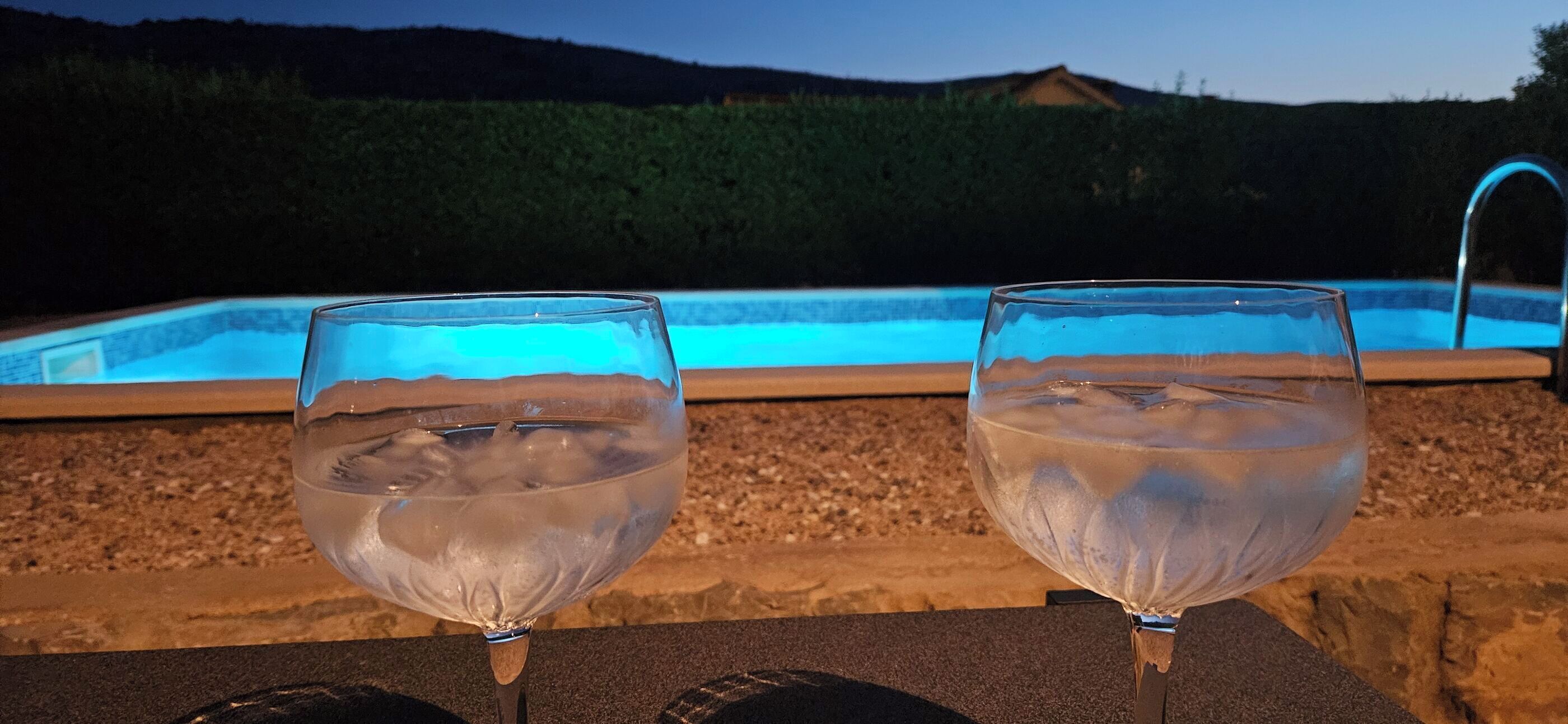 Two glasses of water on a table with a pool in the background.
