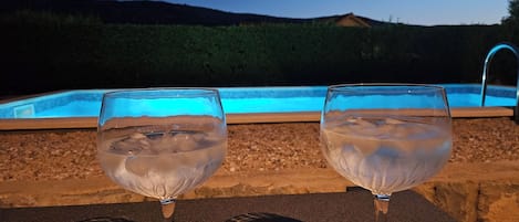 Due bicchieri d'acqua su un tavolo, con una piscina sullo sfondo.