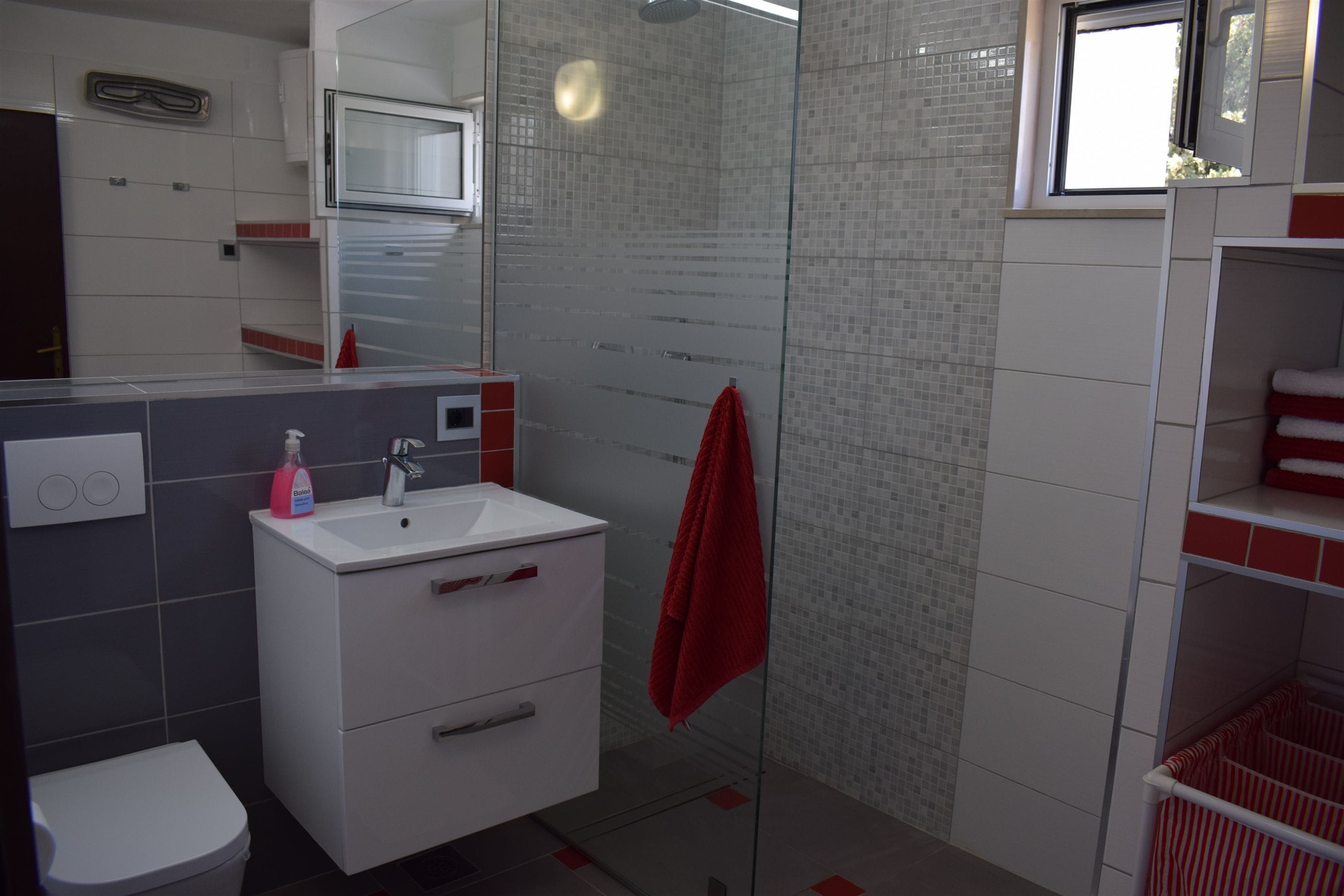 Un baño moderno con cabina de ducha de vidrio, un lavabo blanco y una toalla roja, además de un inodoro.