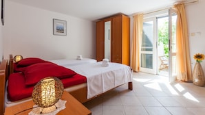Ein Hotelzimmer mit zwei Betten, einem Holzschrank, einem großen Spiegel, einer Schiebeglastür zum Balkon und einer Vase mit einer Sonnenblume.